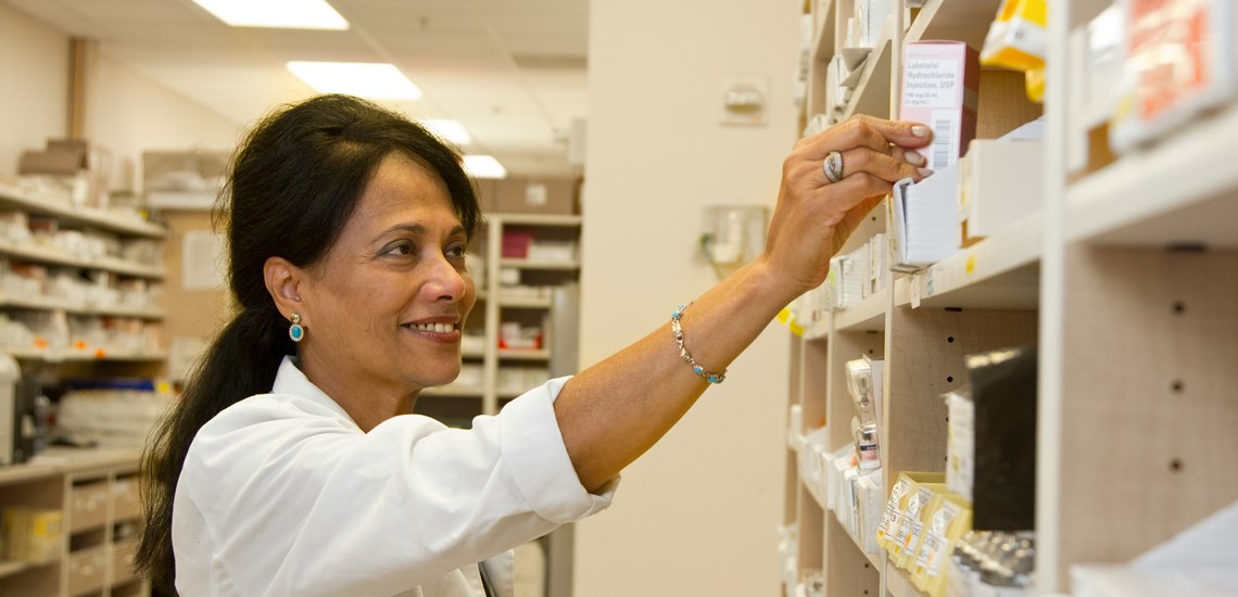 Woman pharmacist taking medication off a shelf 